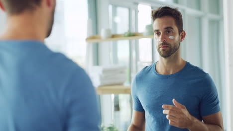 man applying face cream in front of mirror