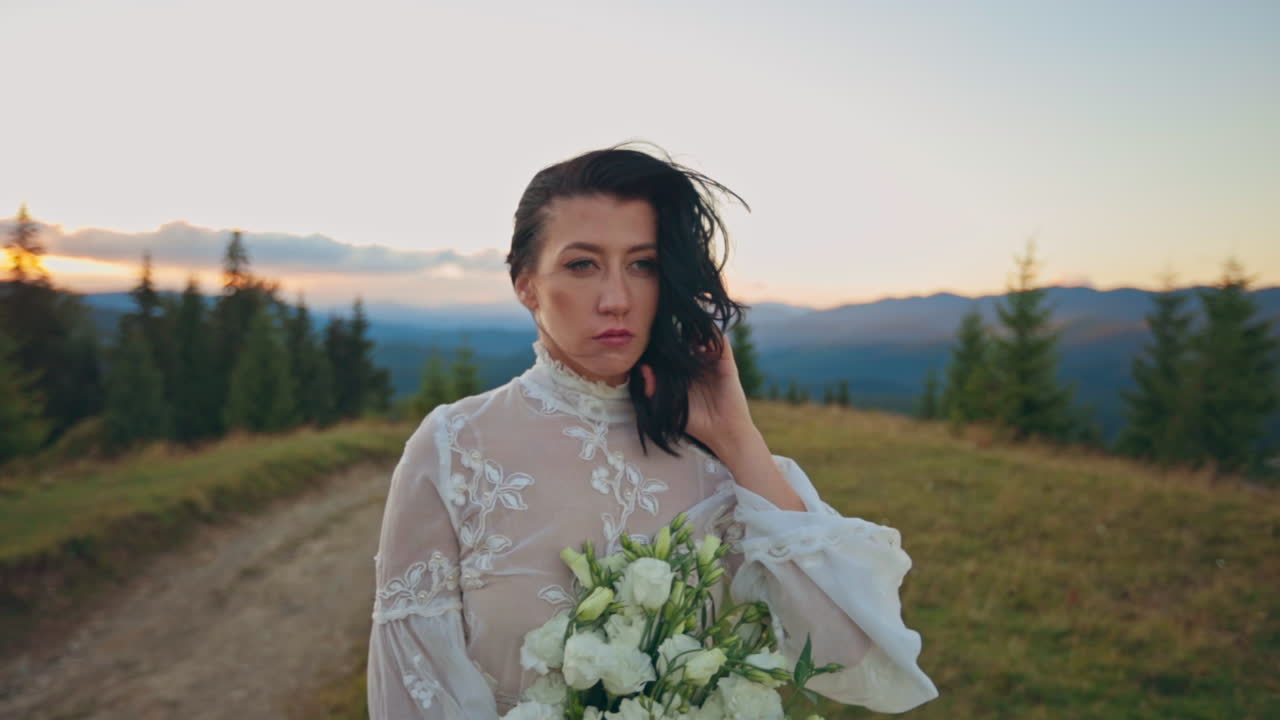 Sposa in abito di pizzo bianco su una cima di montagna al tramonto