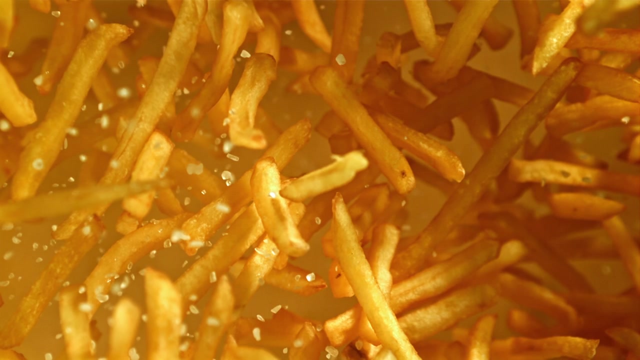Sal espolvoreándose en cámara lenta sobre patatas fritas crujientes y doradas