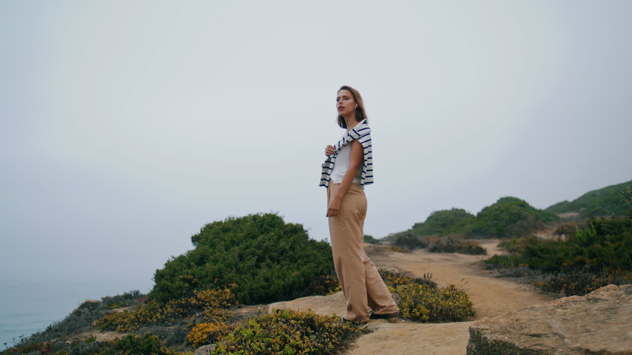 Carefree girl look ocean resting on rocky cliff. Vertical tourist enjoy vacation