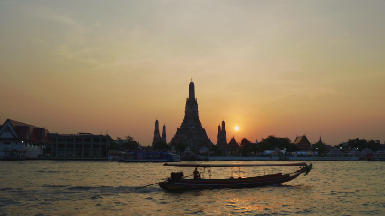 Wat Arun, tempio dell'Alba, a Bangkok, Thailandia, con una barca longtail che passa al tramonto.