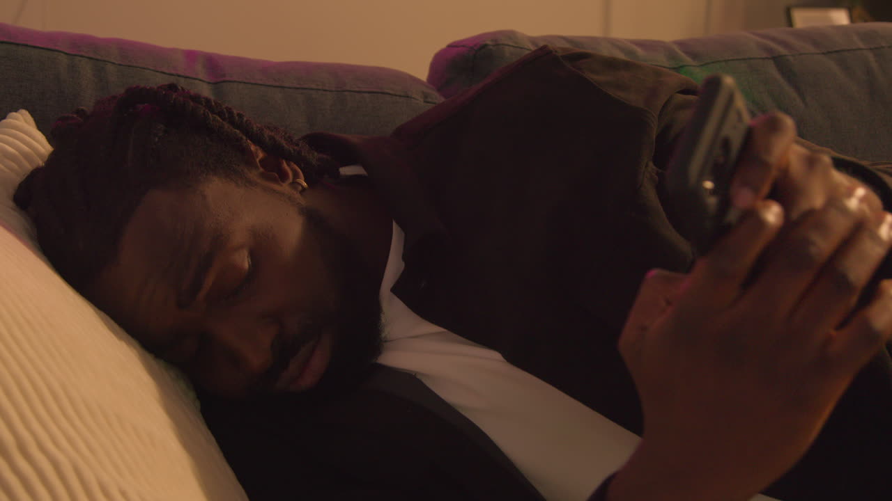 Man Waking Up On Sofa After Drinking Alcohol At House Party Suffering With Hangover Messaging On Mobile Phone 2