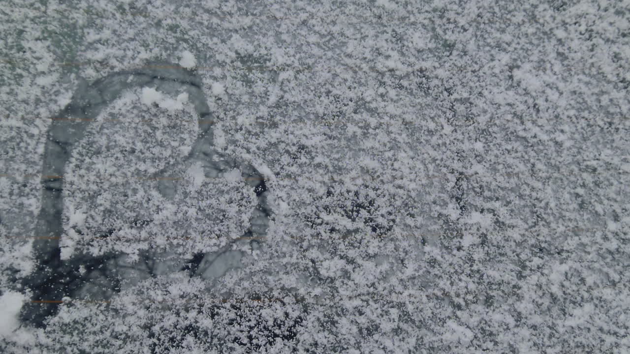 Un primo piano cinematografico di un simbolo del cuore tracciato in uno strato di neve bianca fresca su una finestra o un parabrezza di un'auto. Un simbolo universale di amore e gioia invernale in un'ambientazione realistica del 2026