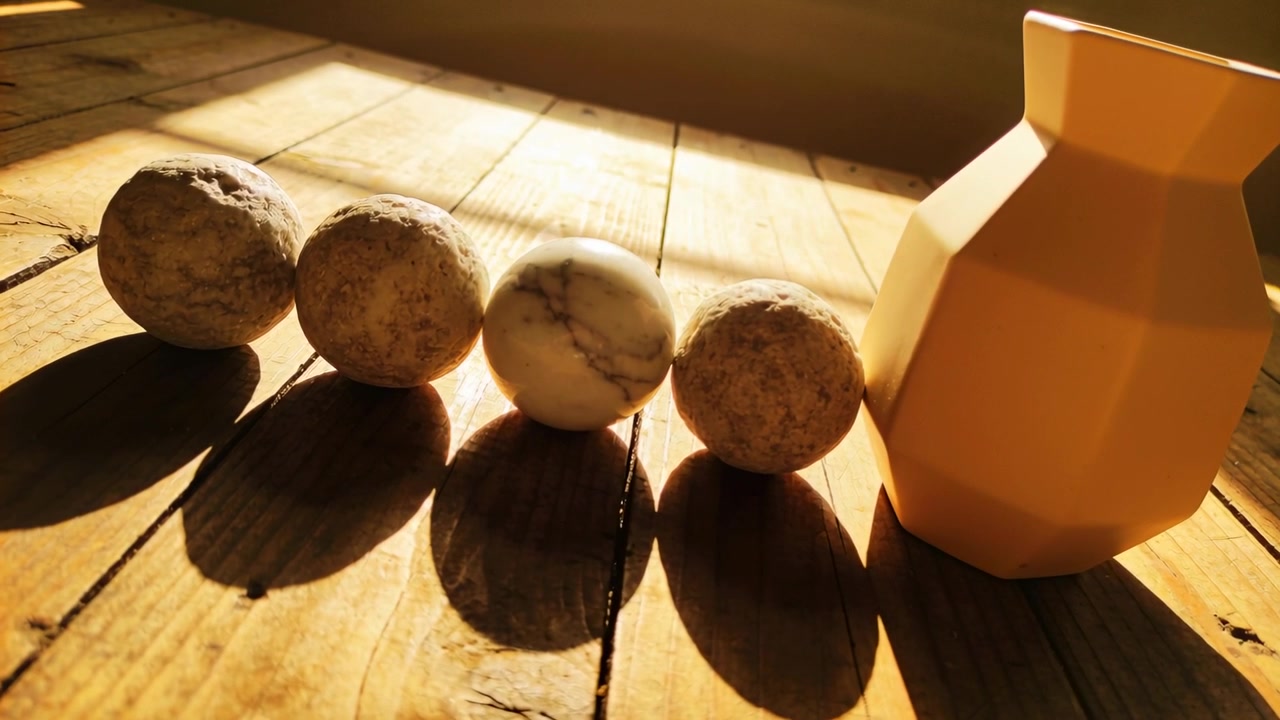 Luce solare serale che proietta lunghe ombre su un tavolo di legno, mostrando quattro sfere e un vaso giallo.
