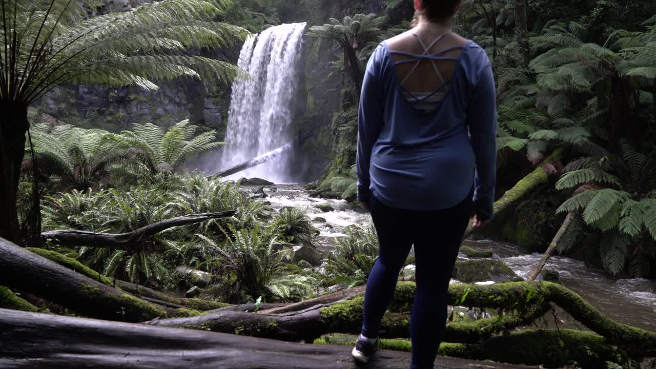 Girl standing in front of waterfall admiring in the forest