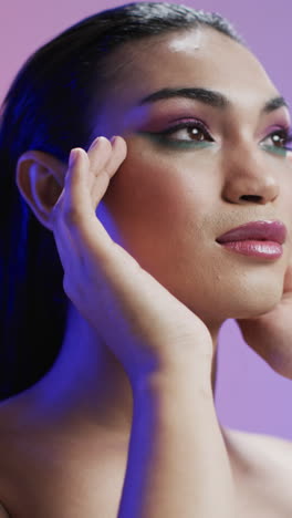vertical video of biracial woman with black hair and make up touching face, copy space, slow motion