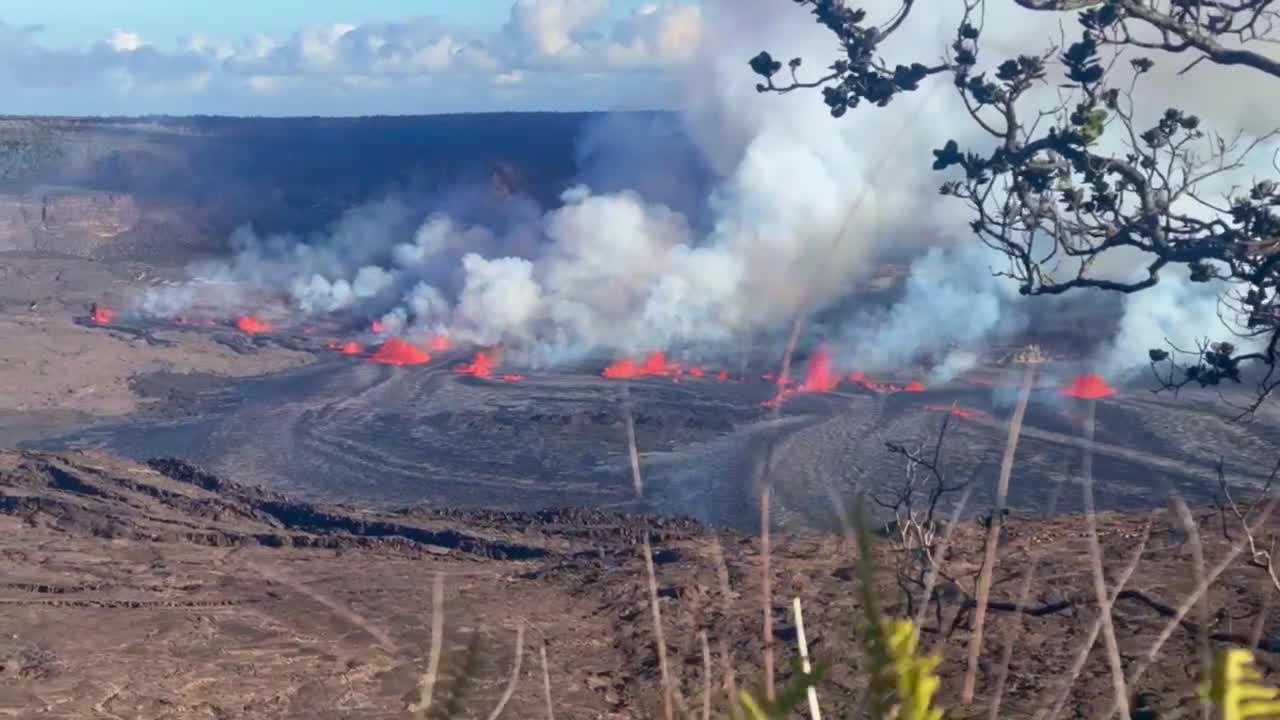 Cinematic long lens shot through foreground plants of Kilauea Volcano erupting in September 2023 on the Big Island of Hawai'i