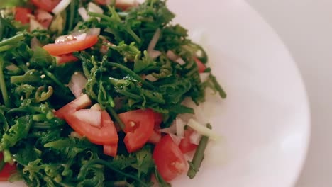 close up overhead shot of seasoning grains dropping to a plate of fiddlehead fern or pako salad, a local filipino delicacy showing the authentic daily home life and heritage