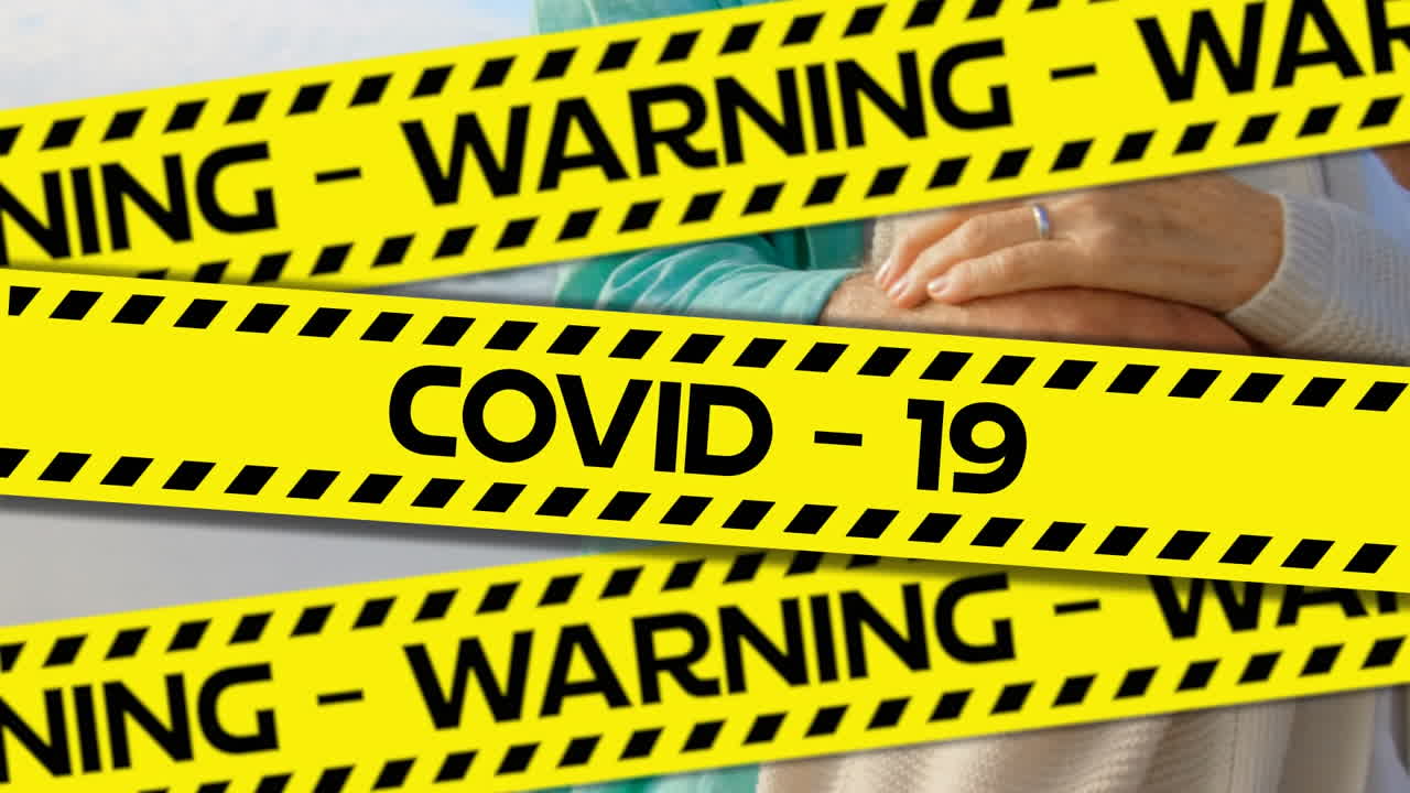 Words Warning Covid-19 written on yellow tape over a senior couple in background. Covid-19 spreading