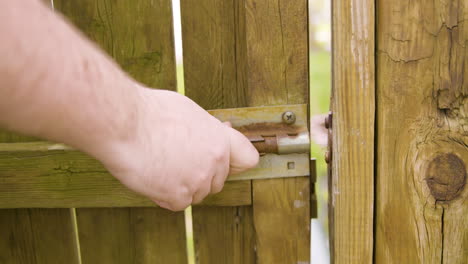 man unlatching old sliding lock and opening gate