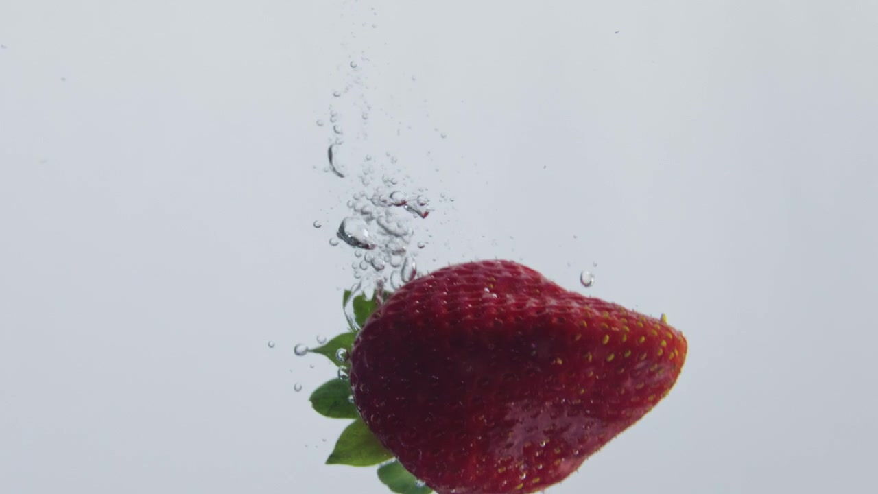 Red strawberry sinking water at white background closeup. Berry dropped liquid.