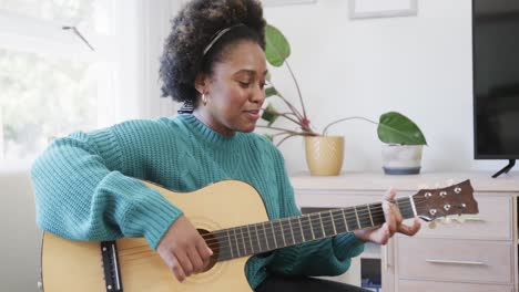 Feliz-Mujer-Afroamericana-Tocando-Guitarra-Y-Cantando-Sentada-En-El-Sofá-En-Casa,-Cámara-Lenta