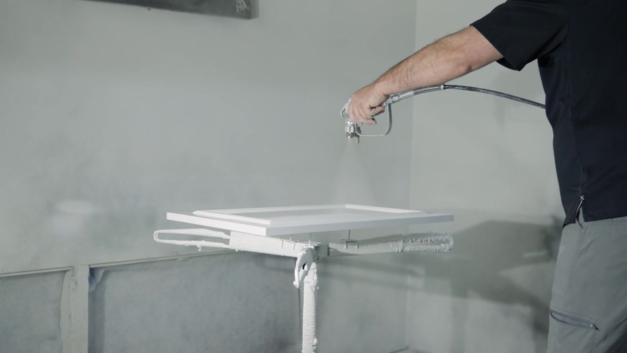 Professional wood worker paints kitchen cabinetry with a paint sprayer in workshop. Perfect for cabinetry, renovation, woodworking, and home improvement visuals.