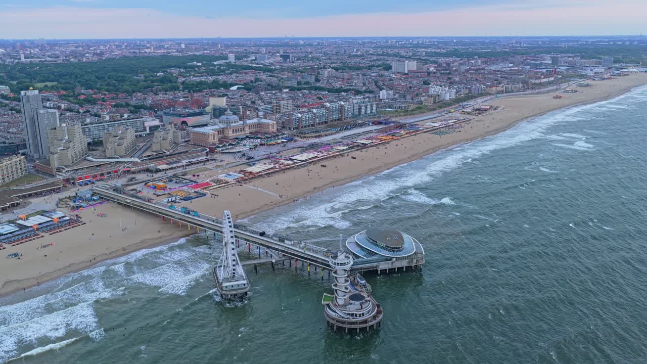 Ripresa aerea al tramonto del Molo di Scheveningen, ruota panoramica e acqua luminosa, Paesi Bassi.