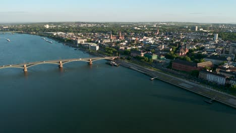 Drohnenflug-über-Der-Mainzer-Biontech-Gründungsstadt-Bei-Tageslicht-Mit-Grünen-Bäumen,-Der-Alten-Brücke-Und-Der-Roten-Kuppel-Im-Hintergrund