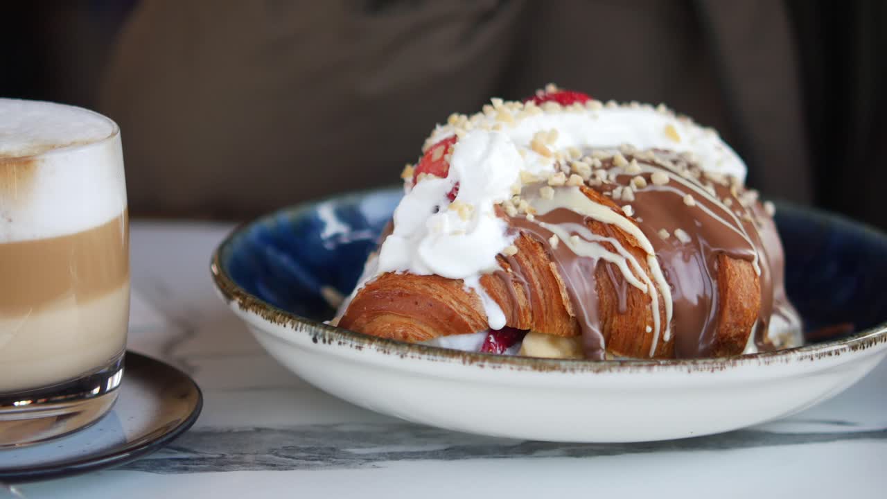 Person eating a chocolate croissant with whipped cream and strawberries