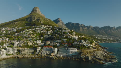 Fliegen-Sie-An-Der-Küste-Entlang,-Die-Von-Luxusimmobilien-Und-Hotels-Gesäumt-Ist.-Rock-Mountain-Ridge-Im-Hintergrund.-Kapstadt,-Süd-Afrika