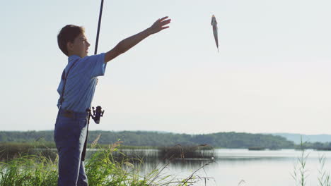 small caucasian boy fisherman catching a fish on a rod and getting it out of the lake