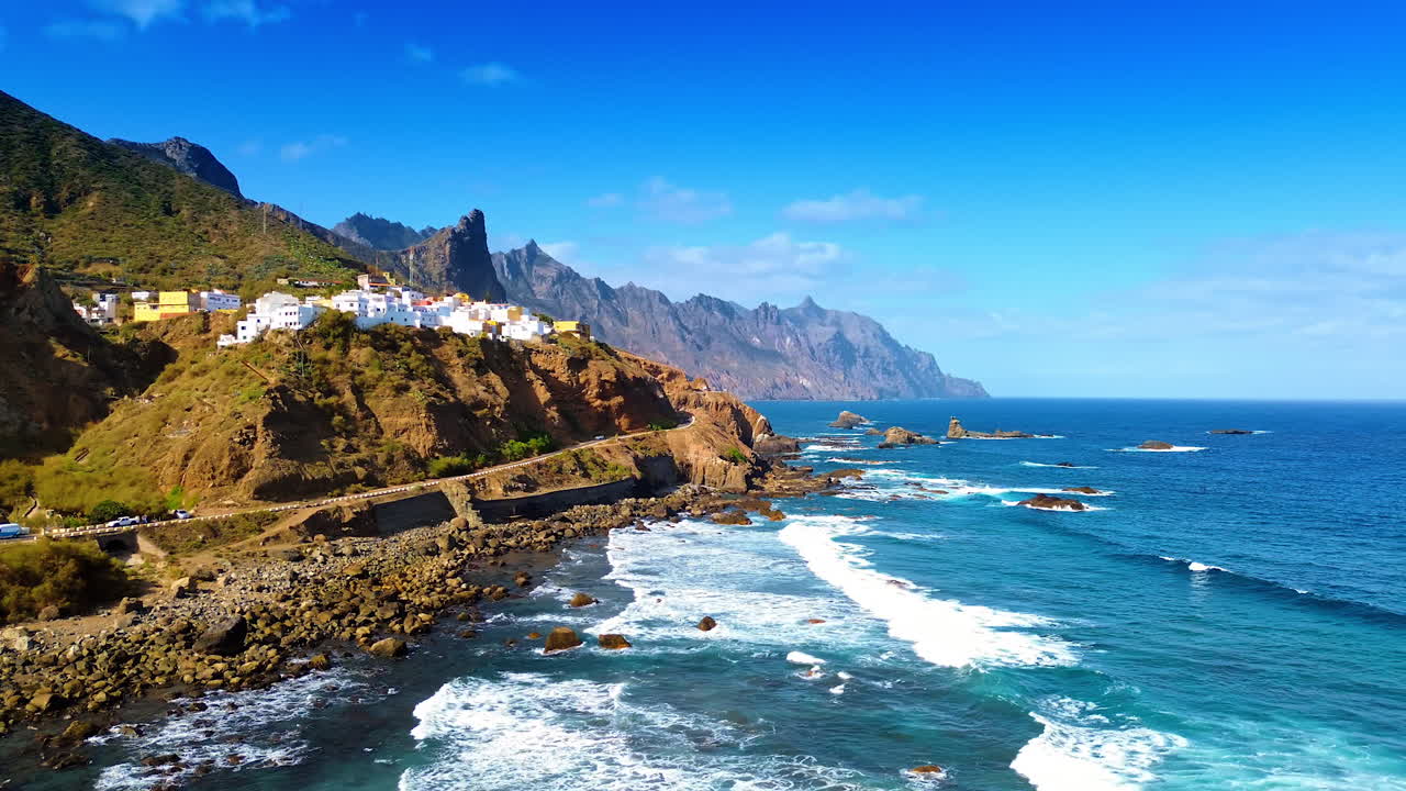 Numerose ville bianche situate sulla costa rocciosa. Bianche onde spumeggianti raggiungono la costa. Tenerife, Isole Canarie, Spagna in una giornata di sole