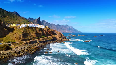 numerous white villas located on the rocky shore. white foamy waves arrive to the coast. tenerife, the canary islands, spain on sunny day