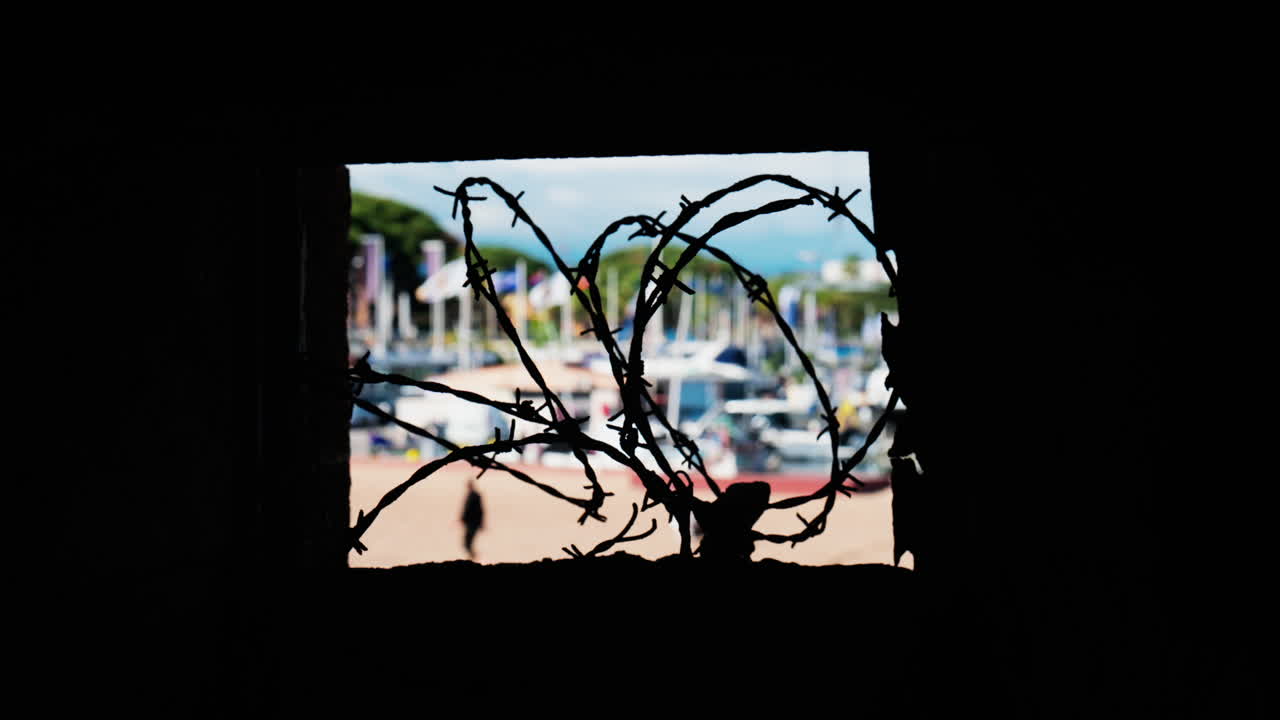Close up of barbed wire loops with a blurred view of boats docked in a harbour in daylight