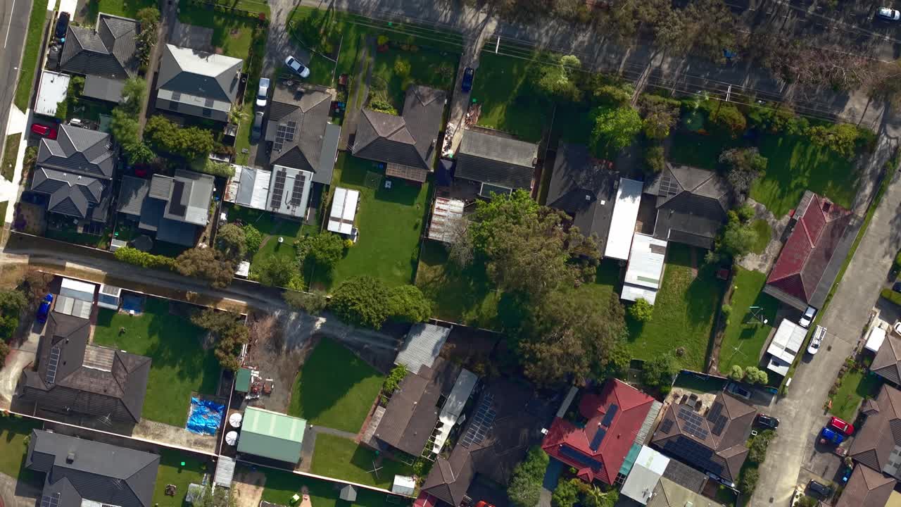 Aerial footage of Liverpool Road in Melbourne captures a tranquil residential suburb. Houses line the street, framed by lush trees, with clear afternoon light casting long shadows