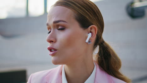 woman wearing earbuds talking sitting urban area close up. lady in earphones