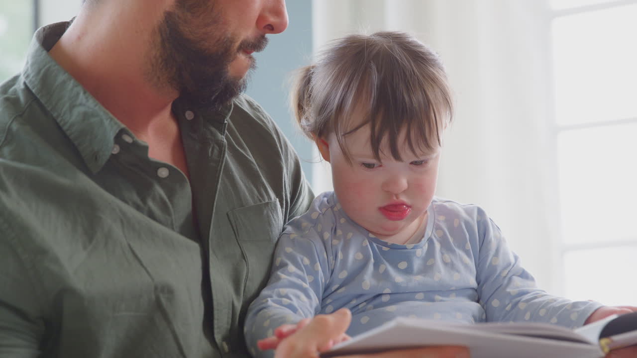 cerca del padre con síndrome de down y la hija leyendo un libro y riendo juntos en casa.