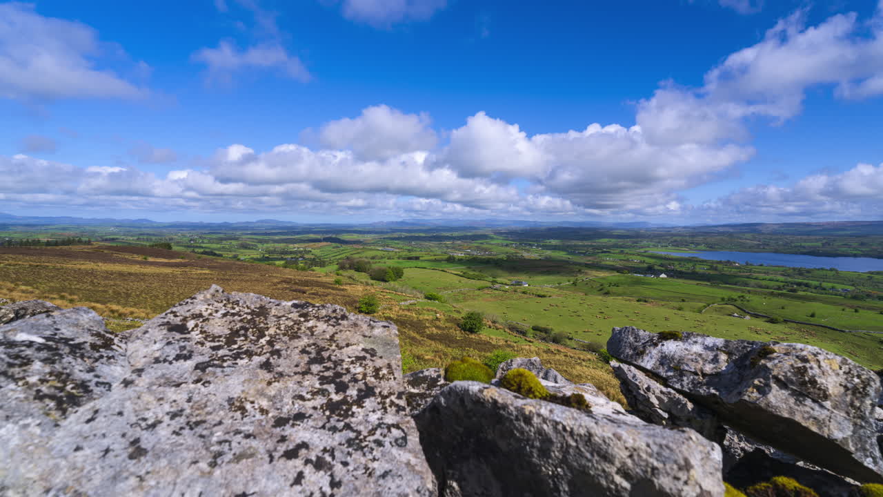 Timelapse af landligt landskab med klippeformation i forgrunden samt bakker og sø i det fjerne p en solrig, skyet dag set fra Carrowkeel i County Sligo i Irland