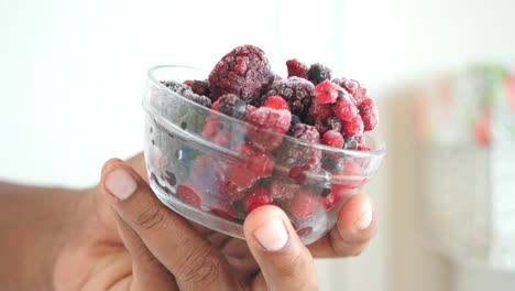 close-up of a hand holding a bowl of frozen mixed berries