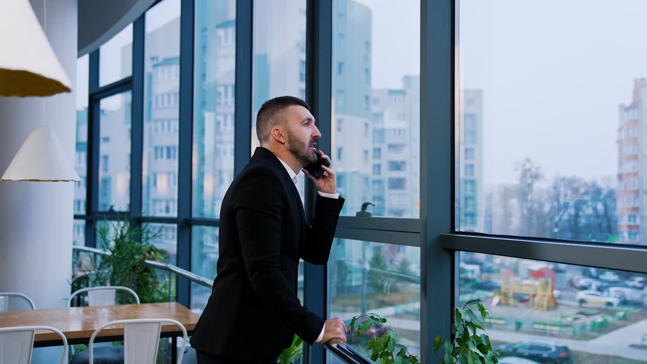 Phone conversation on the phone at office. Man in suit stands at the window holding a phone near his ear.