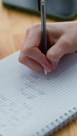 primer plano de la mano de la mujer escribiendo en papel gráfico con pluma, taza de café y teléfono ligeramente borroso en la mesa de madera, creando una atmósfera de espacio de trabajo acogedora y enfocada