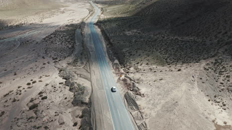 Toma-De-Drone-De-Un-Automóvil-Solitario-Viajando-Por-Una-Carretera-Asfaltada-En-Un-Paisaje-Montañoso-árido-En-Salta,-Argentina