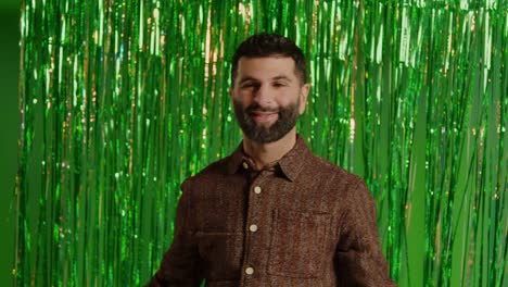 man celebrating st patrick's day standing in front of green tinsel curtain and throwing novelty gold coins in the air