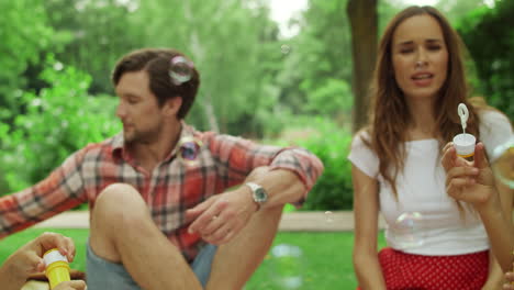 Parents-relaxing-on-blanket-in-park-with-kids.-Children-blowing-soap-bubbles