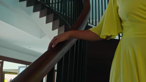 a girl descends the wooden staircase touching the railing with her hand in a yellow long dress