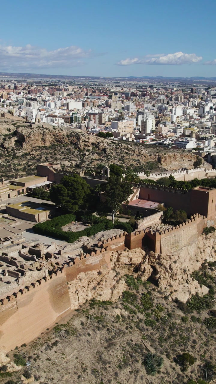 Vertical aerial circling shot of the Alcazaba ruins in Almería, with the cityscape stretching behind.