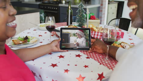 una pareja afroamericana sonriente usando una tableta para una videollamada de navidad con un niño en la pantalla