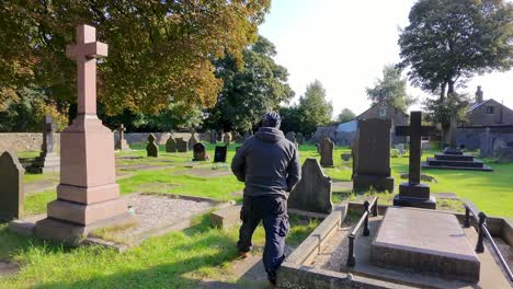 following man wearing hat and casual clothing walking alone in peaceful sunlit cemetery