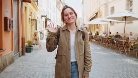 Chica-Turista-Sonriendo-A-La-Cámara-Agitando-Las-Manos-En-Un-Gesto-De-Invitación,-Saludo-En-La-Calle-De-La-Ciudad