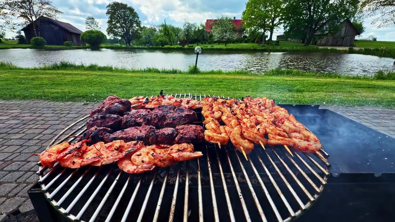 Bir göl kenarında açık hava ızgarasında pişen barbekü karides şişleri ve ızgara et.