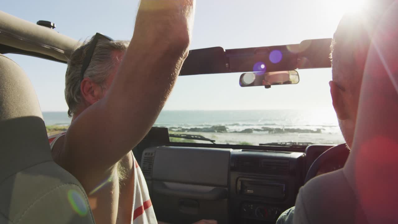 Happy caucasian gay male couple sitting in car and high fiving on sunny day at the beach