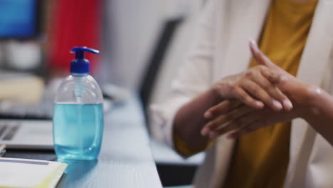 Mid-section-of-woman-sanitizing-her-hands-at-office