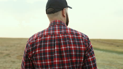 Rear of caucasian farmer wearing a baseball cap walking in the fields