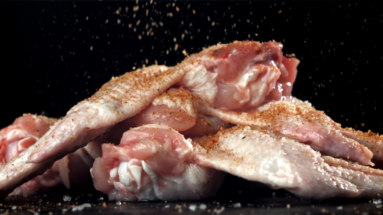 Close-up of Raw Chicken Wings Being Seasoned with Spices