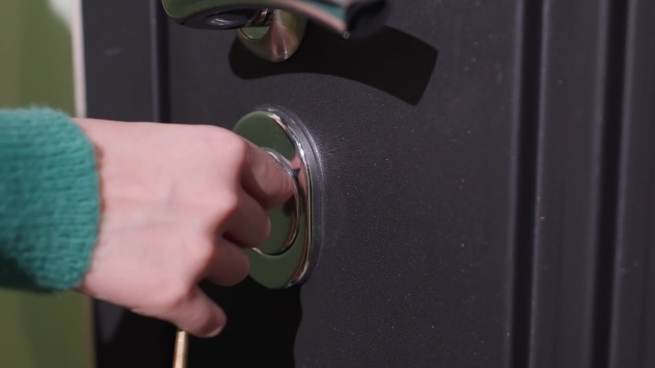 Mano che inserisce la chiave nella serratura, primo piano del catenaccio metallico su porta nera, manica di maglione verde, chiavi d'oro che girano, sbloccare il nuovo appartamento durante il giorno del trasloco, sollievo silenzioso e benvenuto