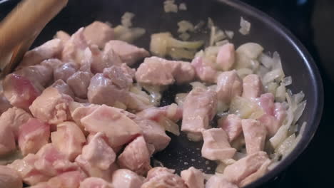 chicken and onions sauteed in hot frying pan, stirred with wooden fork