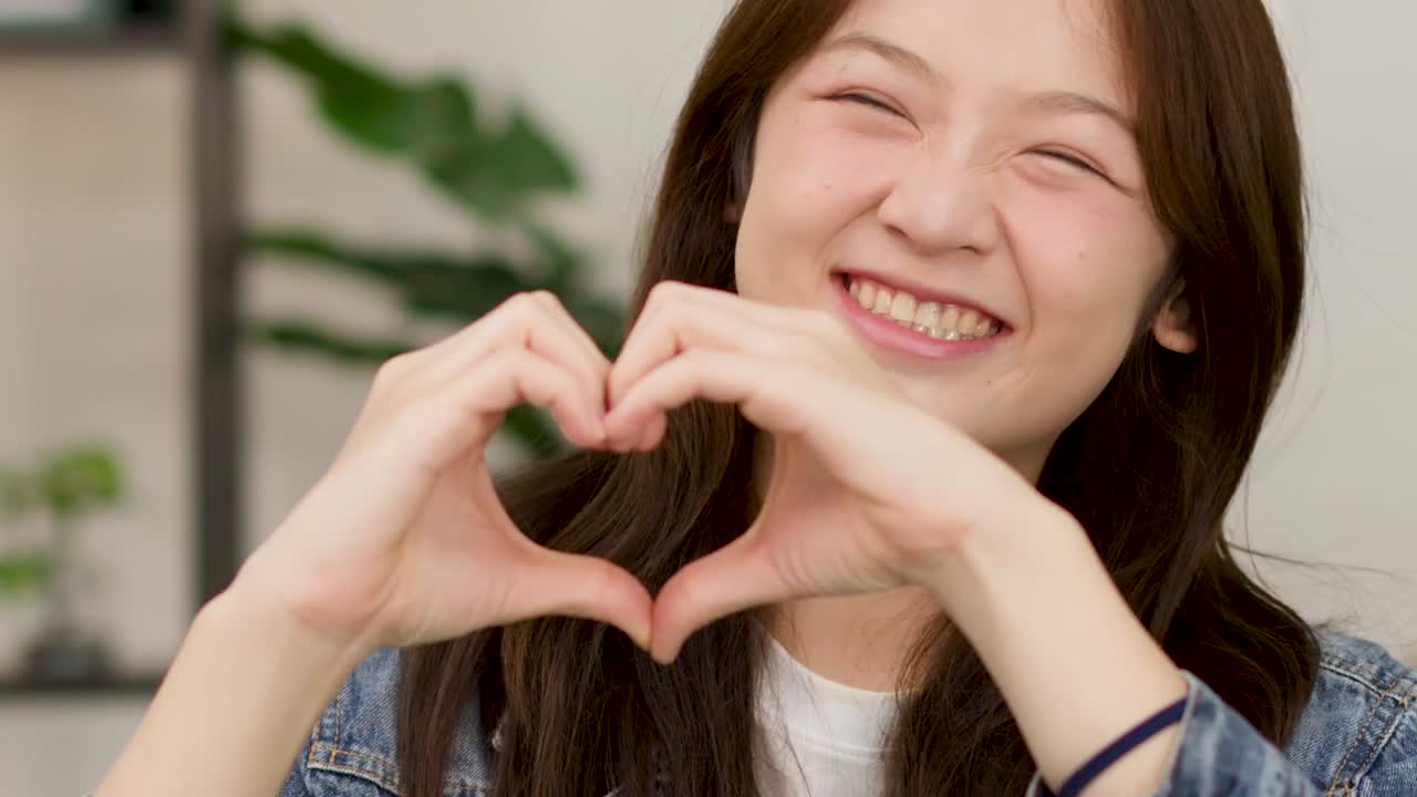 デニムジャケットを着た明るい若い女性が、両手でハート型を作っています。