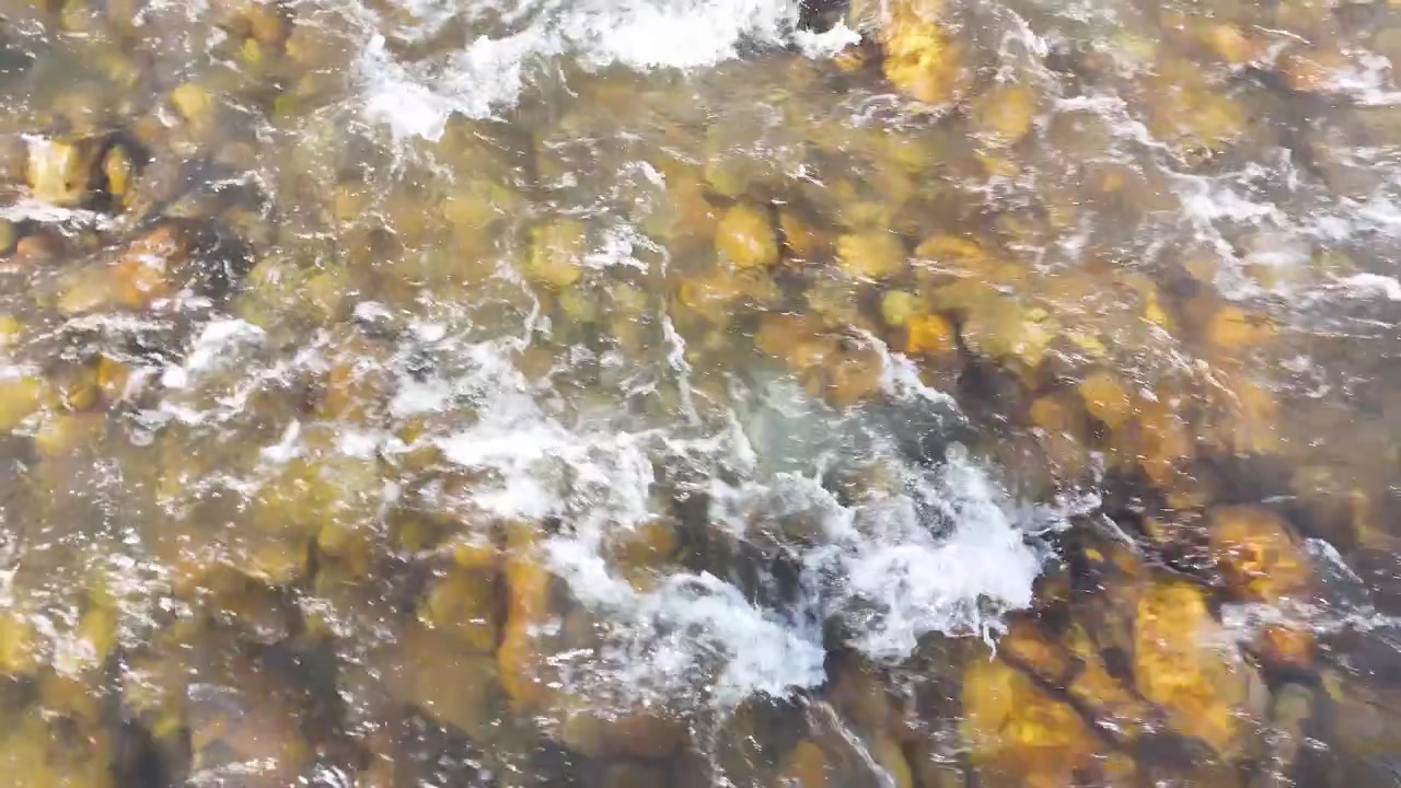 Top-down view of freshwater rushing over submerged rocks and pebbles in a shallow stream.