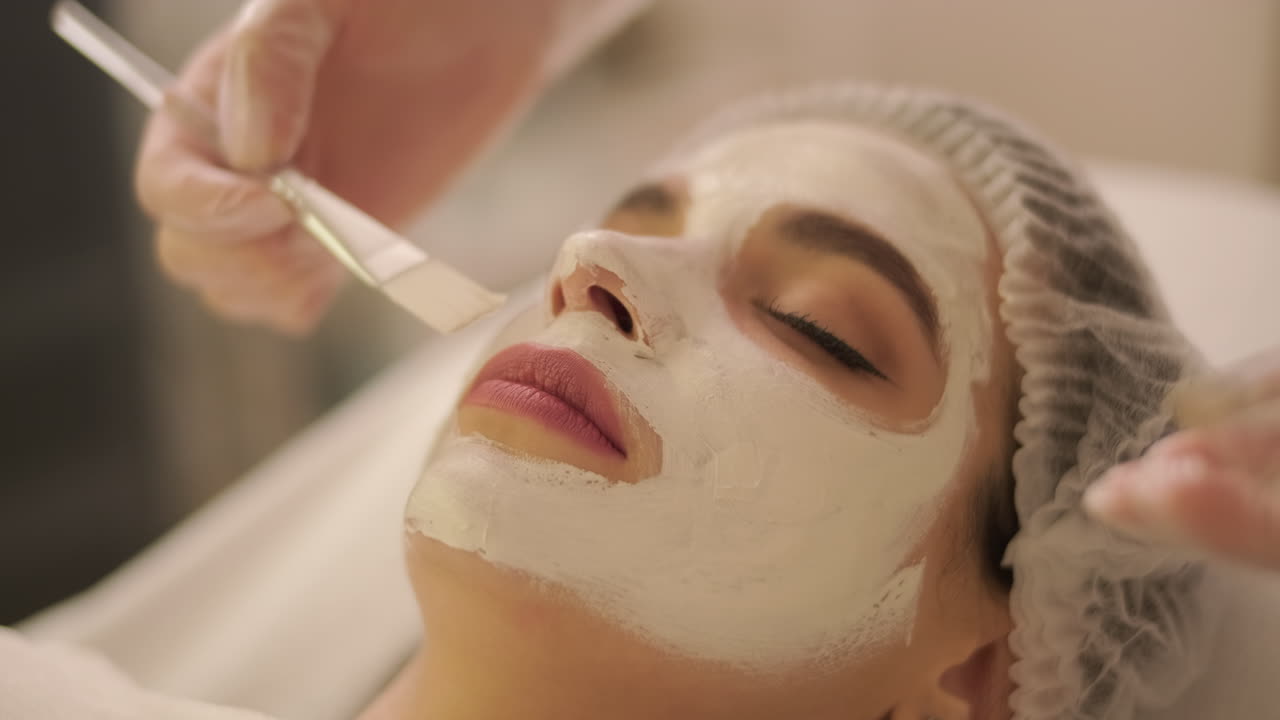 Cosmetologist Applying White Facial Mask to Woman's Face in Spa